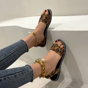Stylish flat leopard print sandals with gold chain and pearl ankle strap detail.