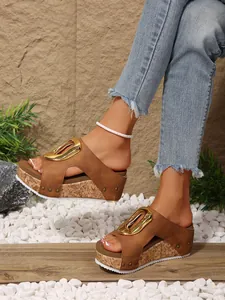 Close-up view of brown wedge platform sandals featuring a large gold buckle and rivet accents