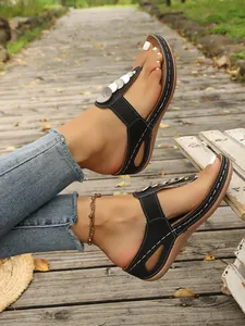 Stylish black wedge flip-flop sandals with metallic disk accents on outdoor boardwalk