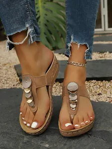 Close-up of stylish camel wedge thong sandals with metallic disc accents on model feet