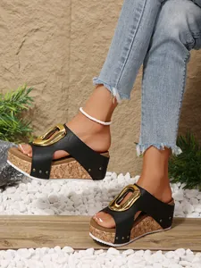 Close-up of black platform wedge sandals with gold buckle and rivet detailing on a model.