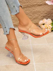 Close-up of orange square-toe sandals with transparent straps and crystal heel