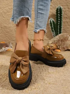 Nahaufnahme von stilvollen braunen Lack-Loafers mit Schleife und dicker Plateausohle.