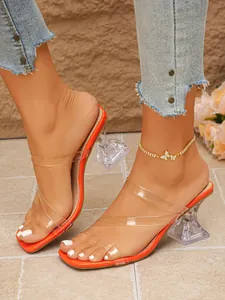 Detail of orange square toe slides with clear straps and transparent wine glass heels.