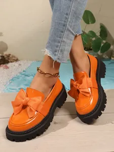 Detailansicht orangefarbene Lackleder-Loafer mit großer Schleife und Plateausohle.