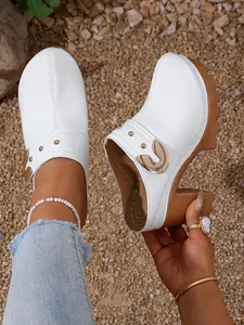 Detail of white patent leather platform clogs with chunky high heels and gold rivets.