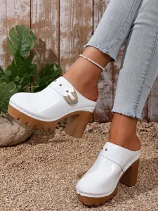Close-up of white high-heeled platform mules with metallic buckle and rivets