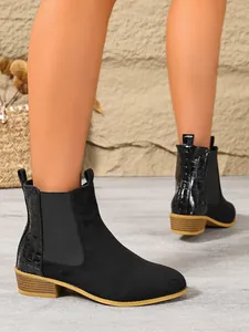 Close-up detail of black suede Chelsea boots featuring croc-embossed heel and block heel design