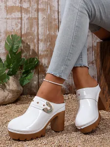 Close-up of white patent leather platform mules with rivet details and brown heels.