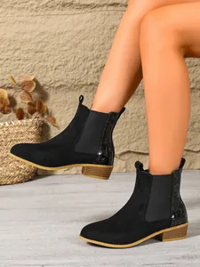 Close-up of black suede Chelsea boots with faux-crocodile heel detail shown on model legs