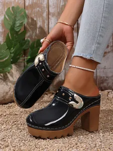 Detail of black patent leather platform mules with gold buckle and rivets.