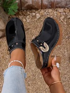 Detailed view of black patent leather platform clogs with rivets and contrast stitching