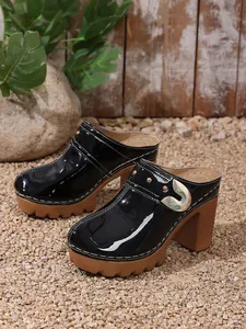 Close-up of black patent leather platform clogs with chunky heel and rivet detail