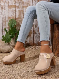 Nude patent leather closed-toe platform mules with chunky high heels on gravel.