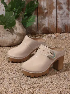 Detailed side view of beige platform mules with decorative gold rivets on gravel