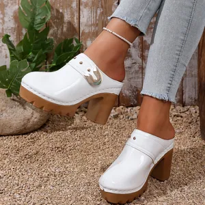 Detail of white patent leather platform mules with chunky high heels and rivet accents.