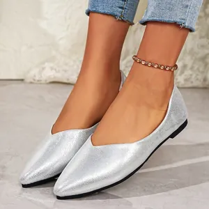 Close-up view of elegant silver pointed-toe flat shoes worn with a beaded anklet.