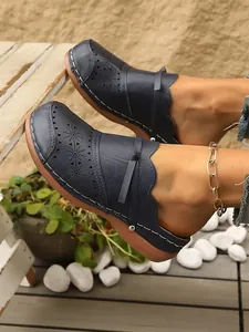 Close-up of navy blue women's retro wedge mules with floral laser-cut detailing.
