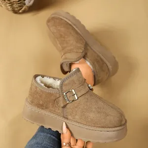 Primer plano de botas de invierno de ante marrón con forro de pelo y hebilla decorativa.