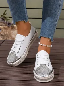 Close-up of stylish white women's sneakers with silver rhinestone toe on wooden floor