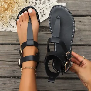 Close-up detail of black T-strap flat sandals with gold buckles shown on wooden floor