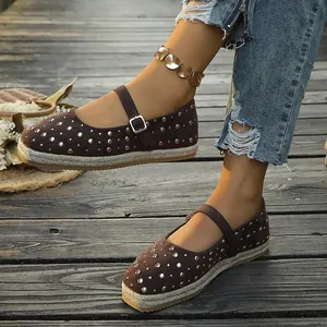 Detailed close-up of brown flat espadrille shoes featuring metallic studs and buckle strap
