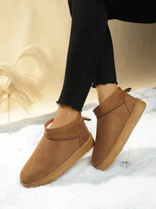 Close-up of classic brown suede snow boots with thick soles on snow