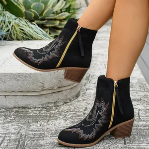Detailed view of black suede western ankle boots with golden embroidery and side zipper.