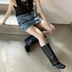 Close-up view of fashionable black tall boots featuring silver rivet accents and wide flaps.