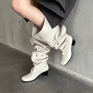 Close-up view of stylish cream leather slouchy boots with metallic studs and block heels