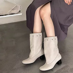 Detail view of chic off-white mid-calf boots with metal eyelets and block heel