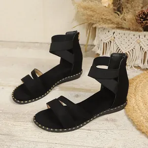 Elegant black sandals with elastic cross ankle straps and back zipper on wooden floor.