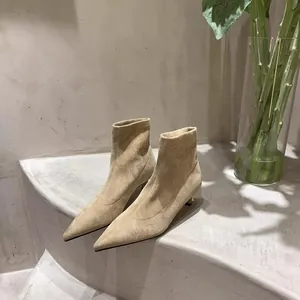 Nahaufnahme beiger Wildleder-Stiefeletten mit spitzer Kappe auf Betontreppen.