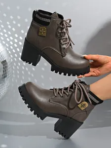 Detailed shot of taupe lace-up ankle boots featuring block heel and vintage metal emblem
