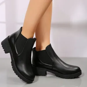 Primer plano de elegantes botines Chelsea negros con tacón grueso y paneles elásticos.