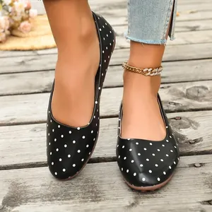 Primo piano di ballerine nere alla moda con pois bianchi indossate da un modello su legno