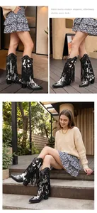 Detailed shot of cow-print cowboy boots featuring black fringe and silver studs.
