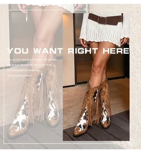 Detailed view of stylish cow print western fringe boots worn by a model in an indoor setting