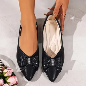 Detailed view of elegant black pointed-toe flat shoes featuring a glittery rhinestone bow.