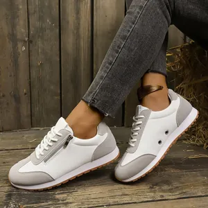 Detailed view of women's white and grey casual sneakers with side zipper on wood