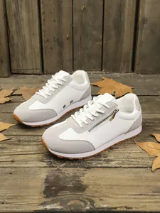 Detailed side view of women's white casual sneakers with decorative zipper on wood