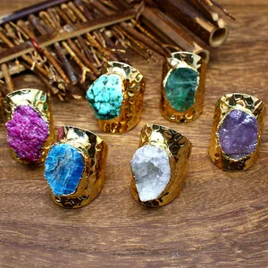 Close-up detail of wide gold-plated rings featuring diverse natural crystal raw stones