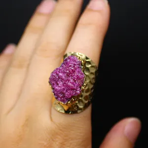 Detailed close-up of a wide gold-tone ring with a rough natural fuchsia raw gemstone