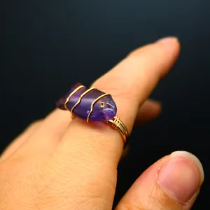 Detailed view of a handmade wire-wrapped ring with carved amethyst fish on a finger.