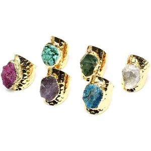 Detailed view of six natural raw stone rings with wide golden hammered bands.