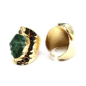 Detailed view of two gold-plated wide band rings with raw natural emerald and quartz stones