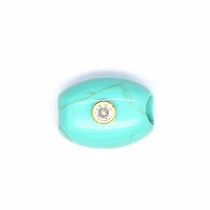 Close-up of turquoise barrel bead jewelry part with centered zircon stone in gold bezel