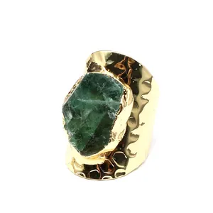 Detailed view of wide gold band ring featuring a raw green crystal stone