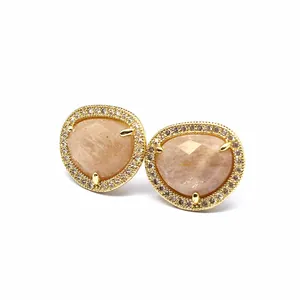 Close-up of faceted natural sunstone stud earrings with gold-plated crystal halo