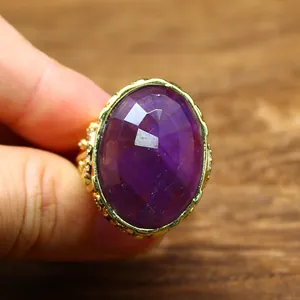 Close-up detail of oversized oval-cut purple crystal ring with ornate gold setting